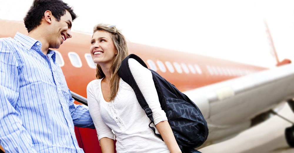 Ett par ler och samtalar framför ett flygplan. De verkar glada och bär på ryggsäckar, antagligen början på en resa.
