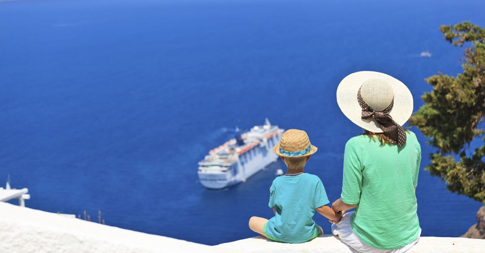 Två personer sitter och tittar ut över havet mot ett kryssningsfartyg, omgiven av blått vatten och himmel.