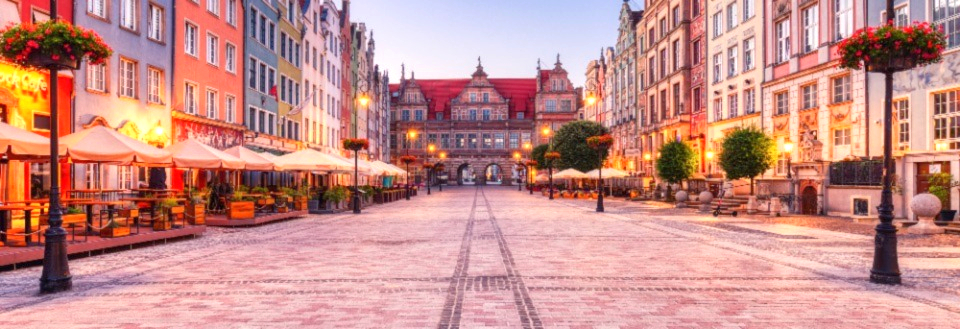 Dlugi Targ i Gdansk i skymningen med traditionell arkitektur, uteserveringar och kullerstensbelagd gata leder mot en dekorerad arkbåge.