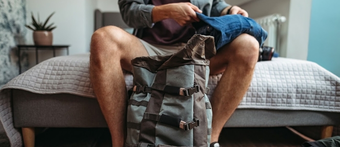 Ung man packar ryggsäck för att besöka staden, förbereder sig på sitt hotellrum
