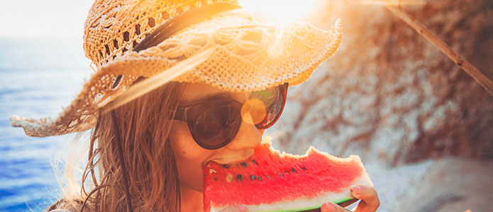 Flicka med solhatt äter en bit vattenmelon i solen
